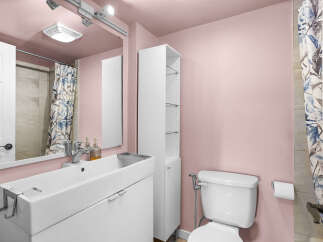 This charming bathroom features a modern white vanity with a sleek sink and chrome faucet, complemented by a tall white storage cabinet for ample space.