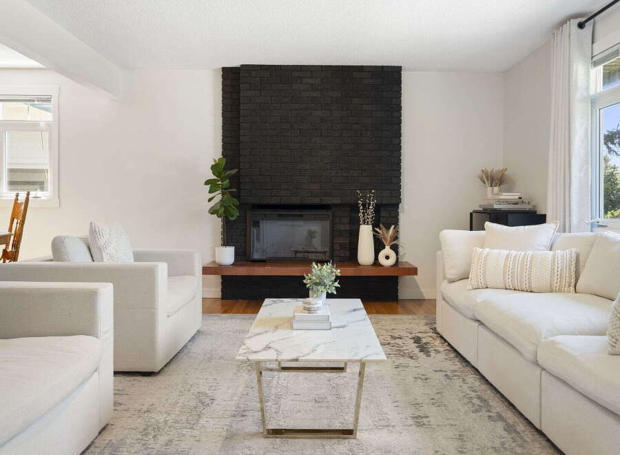 This inviting living room features a striking black brick fireplace as the focal point, complemented by a modern marble coffee table and plush white seating.