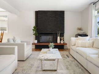 This inviting living room features a striking black brick fireplace as the focal point, complemented by a modern marble coffee table and plush white seating.