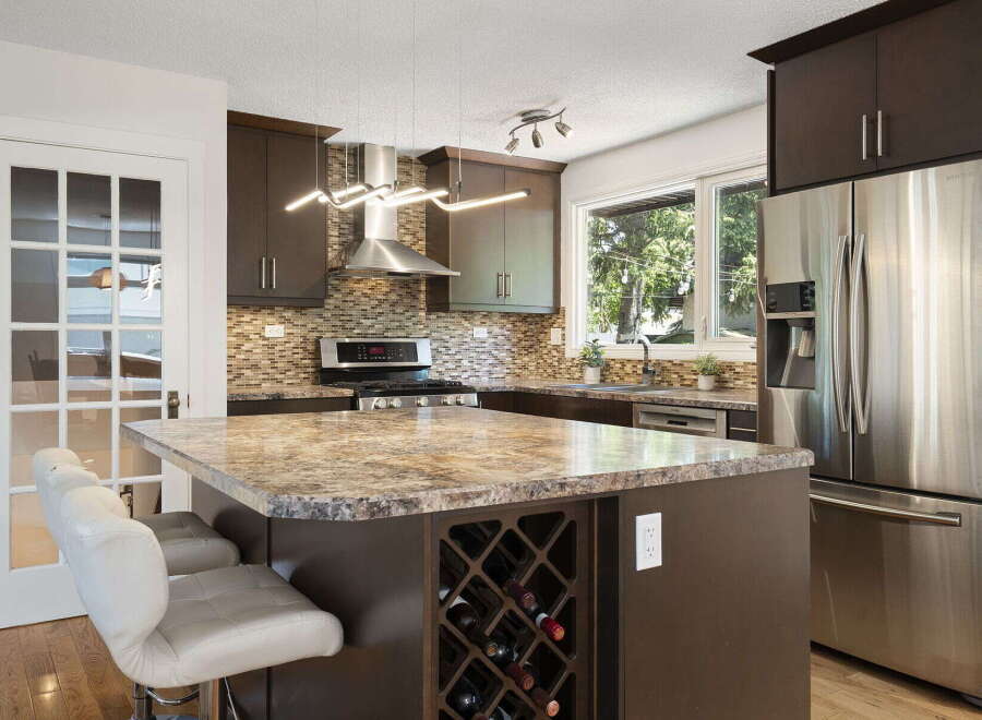 Discover this stunning kitchen featuring dark wood cabinetry, a sleek stainless steel range hood, and a beautiful granite-look countertop island with a built-in wine rack.