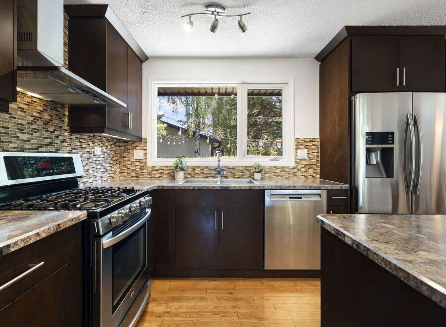 This modern kitchen features dark wood cabinetry, a sleek stainless steel gas range, and a beautiful mosaic tile backsplash.