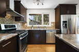 This modern kitchen features dark wood cabinetry, a sleek stainless steel gas range, and a beautiful mosaic tile backsplash.