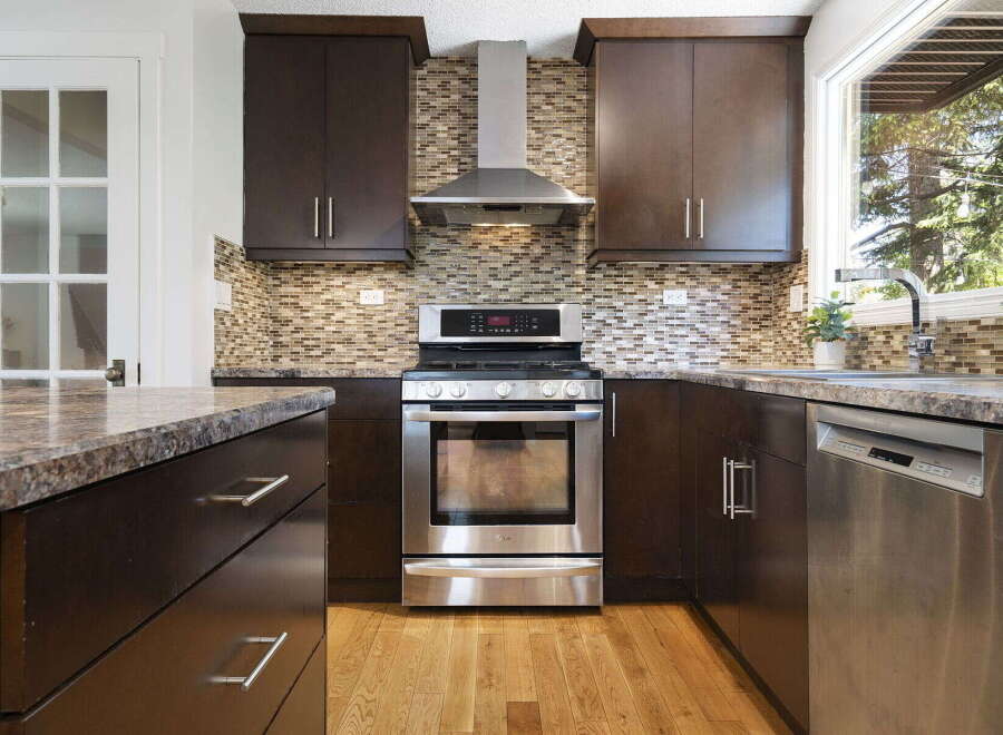 This modern kitchen boasts dark wood cabinetry and a sleek stainless steel range, complemented by a stylish mosaic tile backsplash.