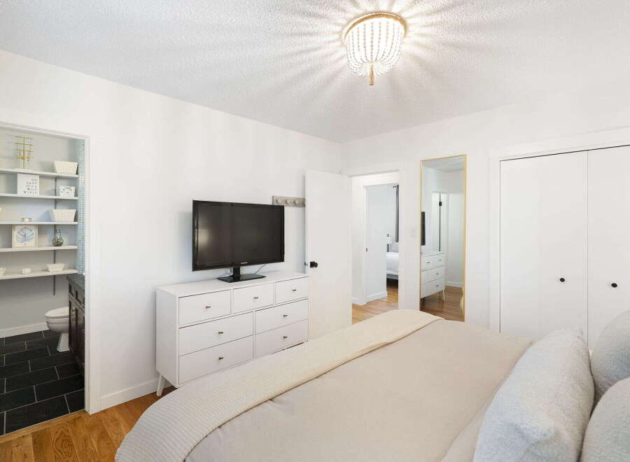 This charming bedroom features a modern white dresser with a flat-screen TV, complemented by a stylish beaded chandelier.