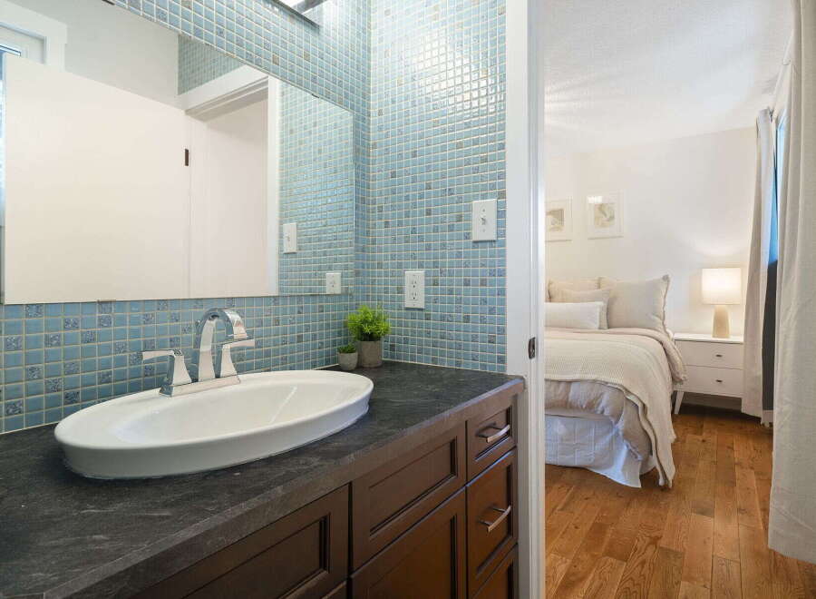 This charming bathroom features a sleek vanity with a modern faucet and a vessel sink, complemented by a striking blue mosaic tile backsplash.
