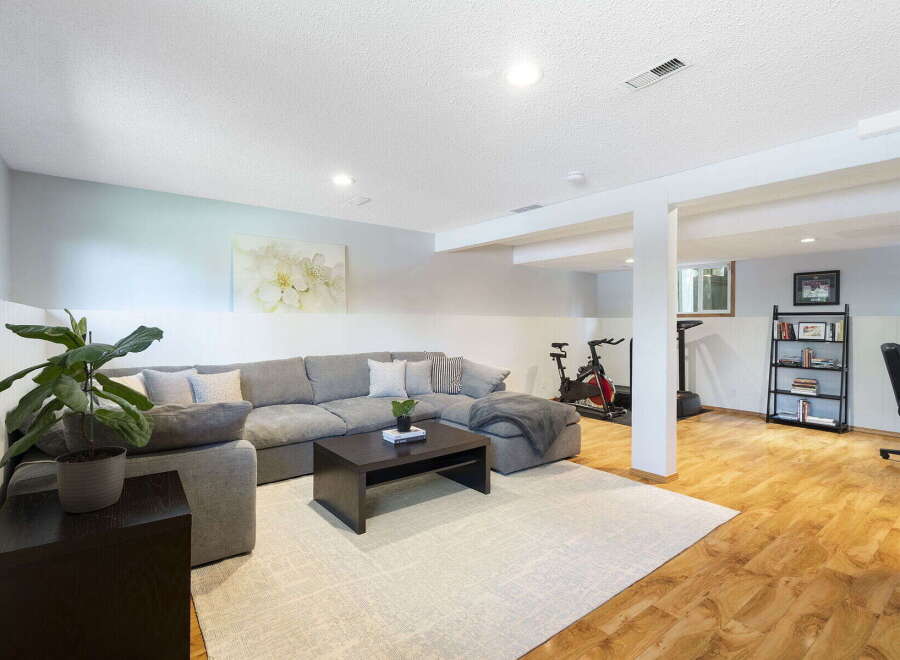 This finished basement offers a versatile living space with a comfortable sectional sofa and a dedicated home gym area featuring a stationary bike and treadmill.