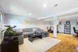 This finished basement offers a versatile living space with a comfortable sectional sofa and a dedicated home gym area featuring a stationary bike and treadmill.