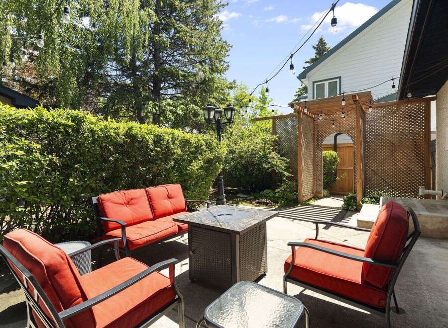 Enjoy outdoor living in this charming backyard oasis, complete with a cozy seating area featuring vibrant red cushions and a stylish fire pit table.