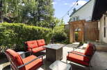 Enjoy outdoor living in this charming backyard oasis, complete with a cozy seating area featuring vibrant red cushions and a stylish fire pit table.