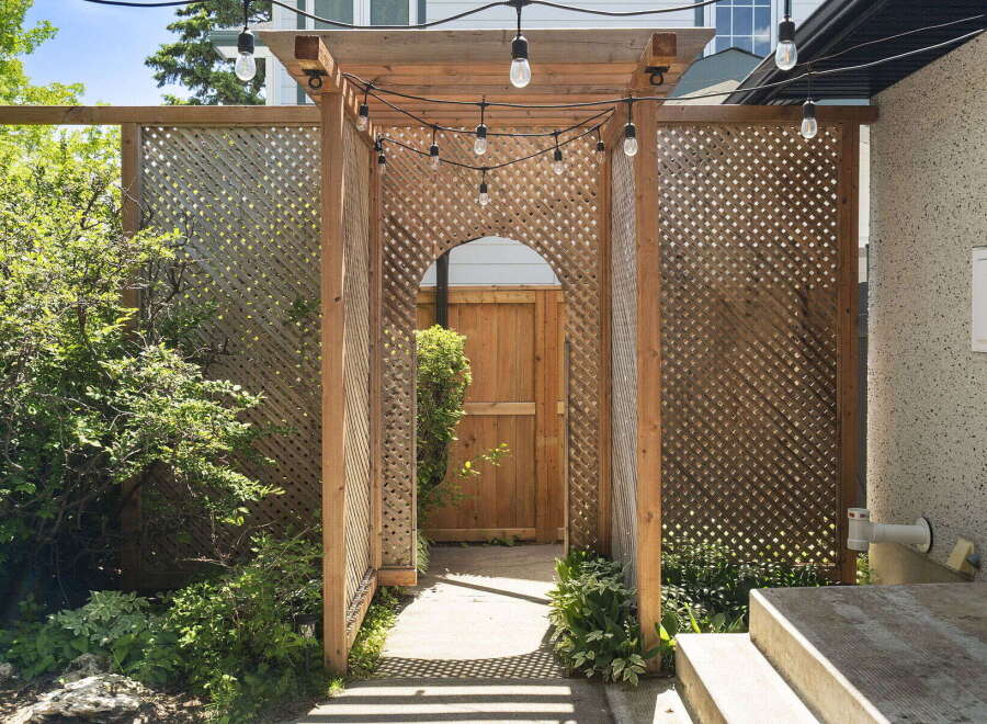 Enhance your outdoor living space with this charming wooden arbor, featuring decorative lattice panels and ambient string lights.