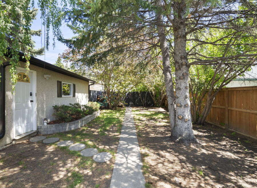 Step into this charming backyard, featuring a welcoming pathway leading through lush greenery and mature trees.