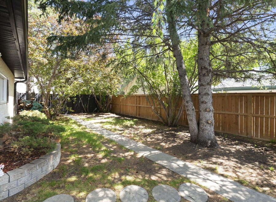 Enjoy the outdoors in this charming backyard featuring a paved walkway leading through lush greenery.