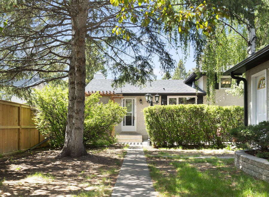 Charming bungalow nestled under mature trees, offering a welcoming facade with a covered entryway and lush landscaping.