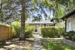Charming bungalow nestled under mature trees, offering a welcoming facade with a covered entryway and lush landscaping.