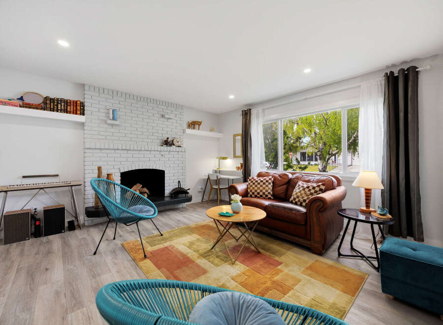 Step into this inviting living room, featuring a cozy brick fireplace and a large window offering a view of the lush outdoors.