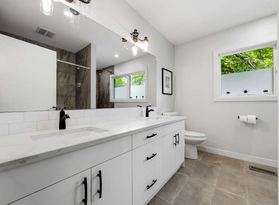 This modern bathroom features a sleek white double vanity with a marble countertop and black fixtures, complemented by a large mirror and subway tile backsplash.