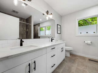 This modern bathroom features a sleek white double vanity with a marble countertop and black fixtures, complemented by a large mirror and subway tile backsplash.