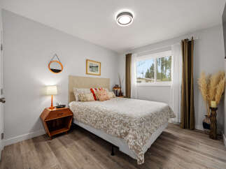 This inviting bedroom features a comfortable queen-size bed with a patterned duvet and decorative pillows, complemented by a textured headboard.
