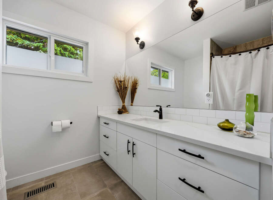 This modern bathroom features a sleek white vanity with black hardware, complemented by a white quartz countertop and subway tile backsplash.