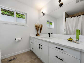 This modern bathroom features a sleek white vanity with black hardware, complemented by a white quartz countertop and subway tile backsplash.