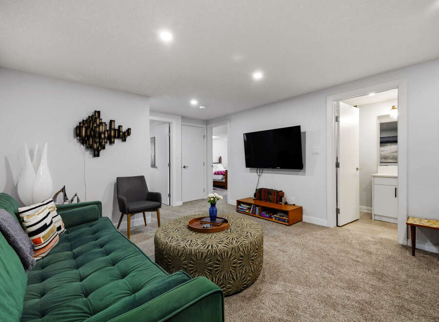 Step into this inviting living space featuring a plush green sofa complemented by a decorative ottoman and a modern wall-mounted TV.