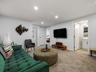 Step into this inviting living space featuring a plush green sofa complemented by a decorative ottoman and a modern wall-mounted TV.
