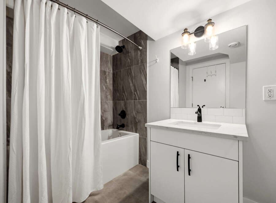 This modern bathroom features a sleek white vanity with a marble countertop and a black faucet, complemented by a subway tile backsplash.