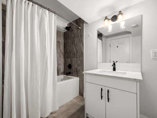 This modern bathroom features a sleek white vanity with a marble countertop and a black faucet, complemented by a subway tile backsplash.
