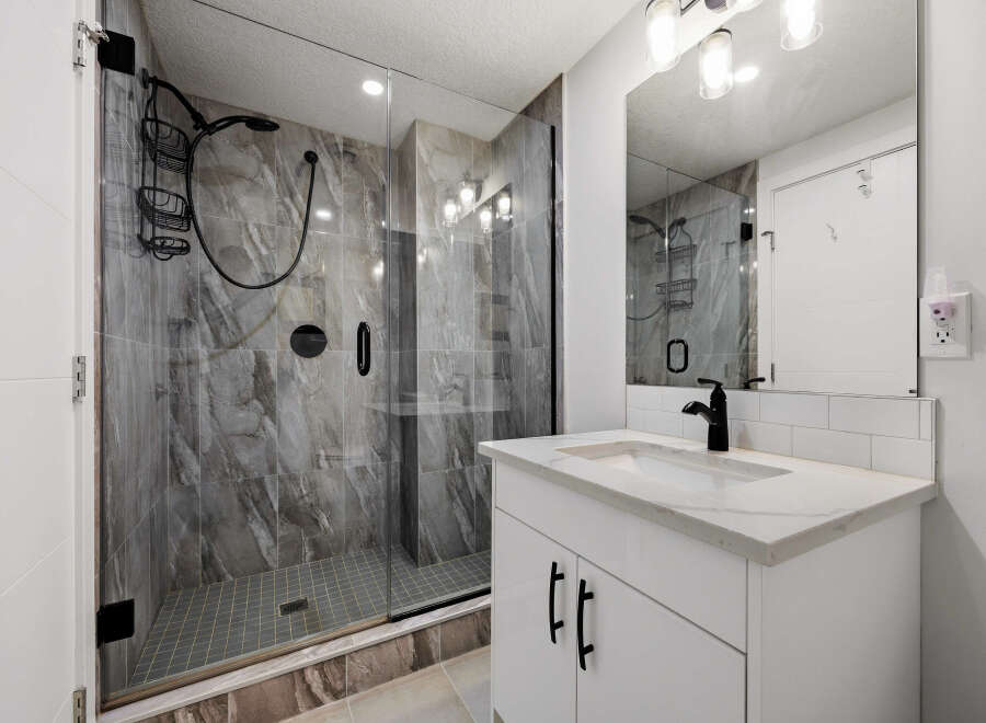 Experience modern luxury in this stunning bathroom, featuring a spacious walk-in shower with elegant marble-look tiles and a sleek black shower system.