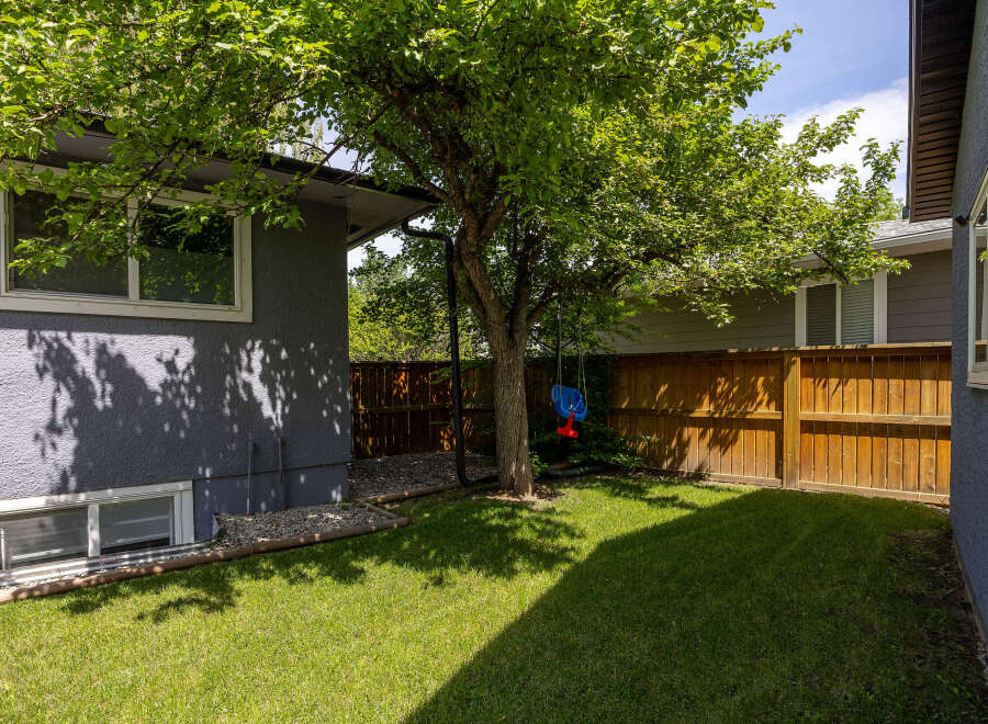 Enjoy outdoor living in this charming backyard featuring a lush green lawn and a mature tree perfect for shade.