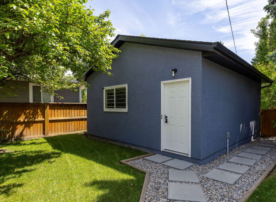 Discover this charming property featuring a detached garage with a modern blue stucco exterior and a white door.