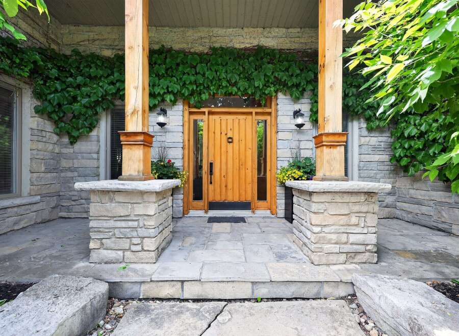Enhance your home's curb appeal with this charming entryway, featuring a beautiful wooden door framed by natural stone and lush greenery.