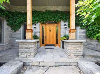 Enhance your home's curb appeal with this charming entryway, featuring a beautiful wooden door framed by natural stone and lush greenery.
