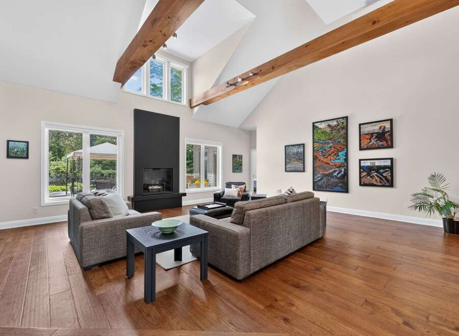 Experience luxurious living in this stunning great room, featuring a dramatic vaulted ceiling with exposed wooden beams and a modern black fireplace as the focal point.