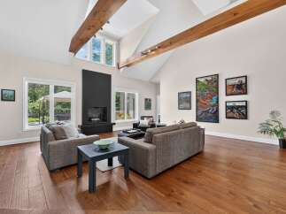 Experience luxurious living in this stunning great room, featuring a dramatic vaulted ceiling with exposed wooden beams and a modern black fireplace as the focal point.