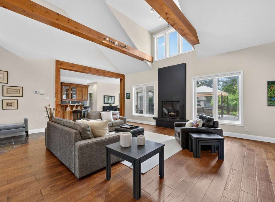 Experience luxurious living in this stunning great room, featuring soaring vaulted ceilings with exposed wooden beams and a modern black fireplace as the focal point.