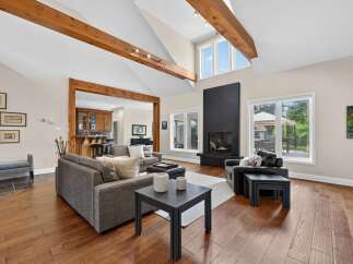 Experience luxurious living in this stunning great room, featuring soaring vaulted ceilings with exposed wooden beams and a modern black fireplace as the focal point.