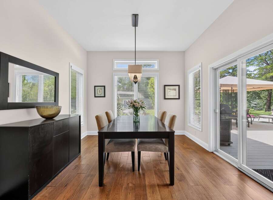 This elegant dining room features a dark wood dining table with upholstered chairs, complemented by a sleek black sideboard and a large wall mirror.