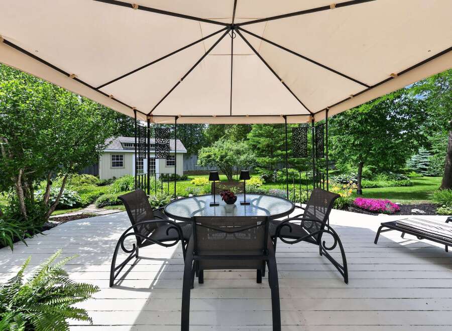 Enjoy outdoor living under this elegant gazebo, featuring a glass-top dining table and four chairs perfect for al fresco meals.