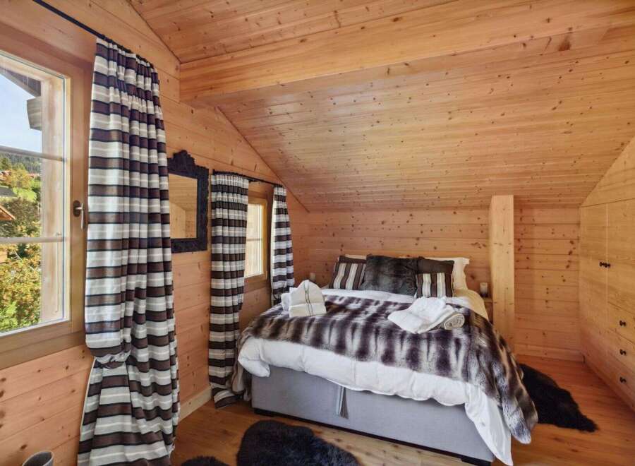 Experience cozy mountain living in this charming chalet bedroom, featuring a plush faux fur throw and warm wood paneling throughout.