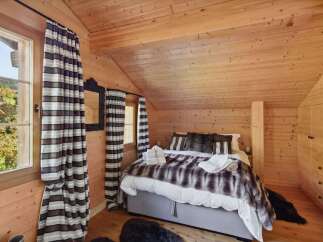 Experience cozy mountain living in this charming chalet bedroom, featuring a plush faux fur throw and warm wood paneling throughout.