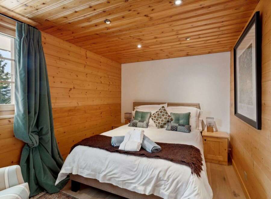 Experience cozy mountain living in this charming bedroom featuring warm wood-paneled walls and ceiling.