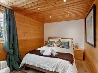Experience cozy mountain living in this charming bedroom featuring warm wood-paneled walls and ceiling.