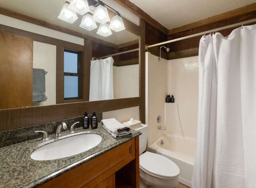 This rustic bathroom features a granite-topped vanity with a undermount sink and a wooden cabinet below.