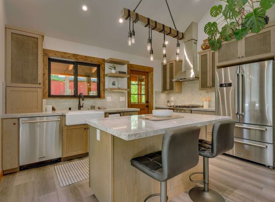 Experience rustic charm in this beautifully appointed kitchen, featuring a large farmhouse sink, a spacious island with granite countertops, and a striking wooden beam light fixture.
