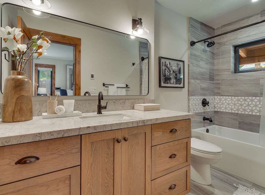 This modern bathroom features a warm wood vanity with ample storage and a sleek quartz countertop.