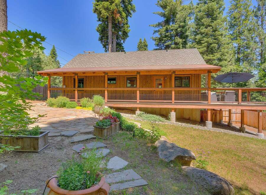 Charming wooden cabin nestled among tall trees, featuring a spacious wrap-around porch perfect for enjoying the serene surroundings.