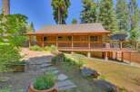 Charming wooden cabin nestled among tall trees, featuring a spacious wrap-around porch perfect for enjoying the serene surroundings.