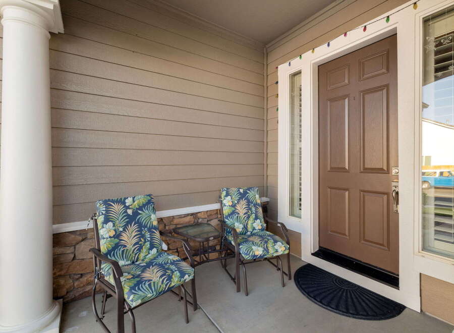 Welcome guests to your charming home with this inviting front porch, featuring two comfortable chairs with tropical-themed cushions and a convenient side table.