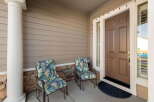 Welcome guests to your charming home with this inviting front porch, featuring two comfortable chairs with tropical-themed cushions and a convenient side table.
